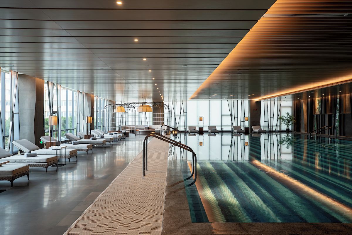A modern indoor swimming pool area with lounge chairs and a glass barrier.