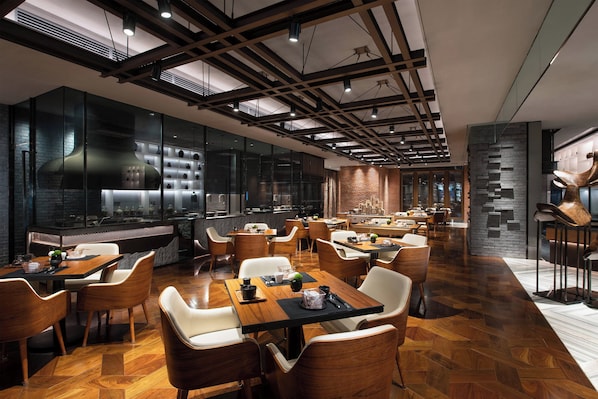 Un restaurante moderno con mesas y sillas de madera, una amplia zona de cocina y una pared de ladrillo.