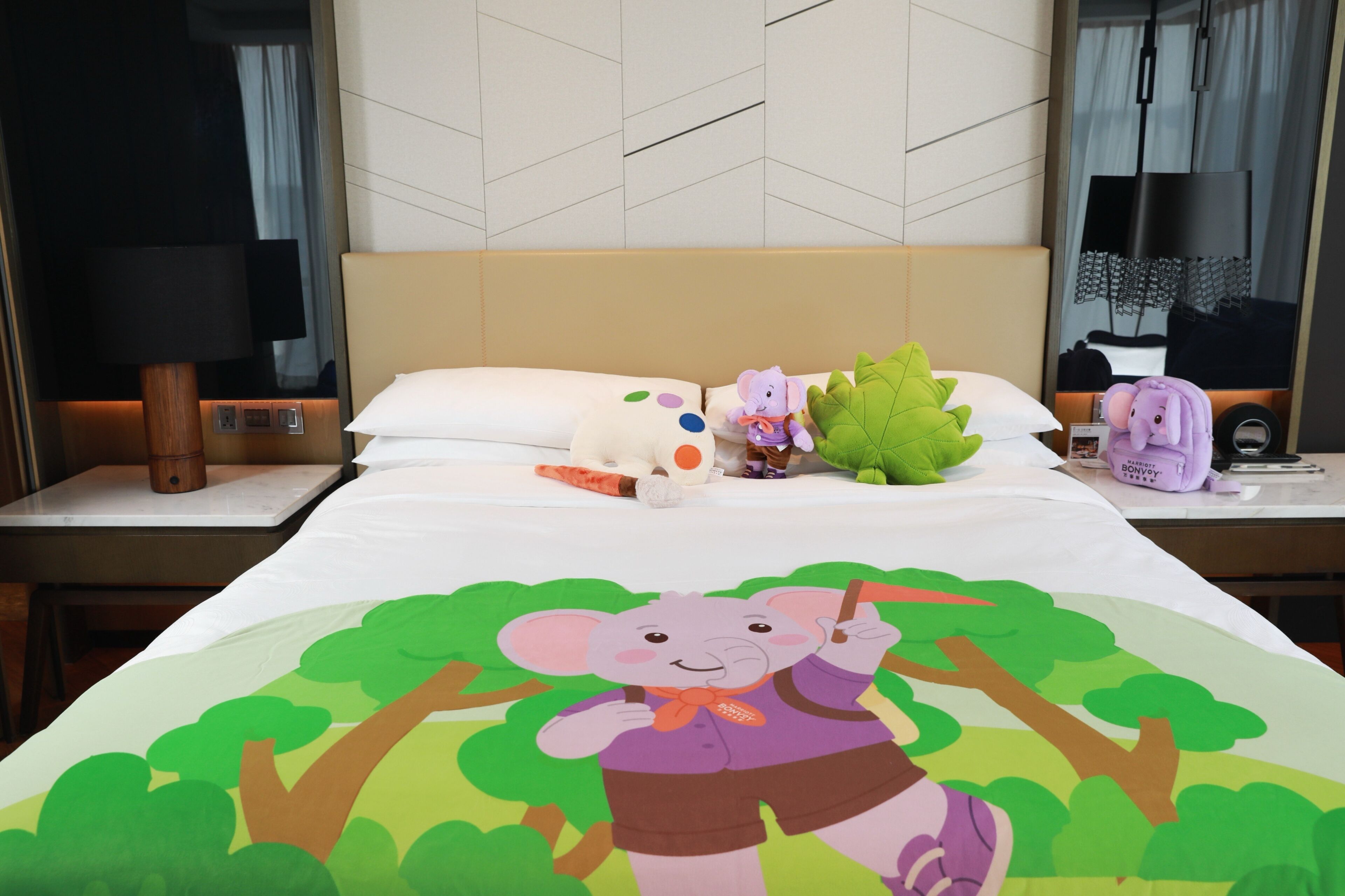 A hotel room with a bed, a nightstand, a lamp, a mirror, and a plush toy.