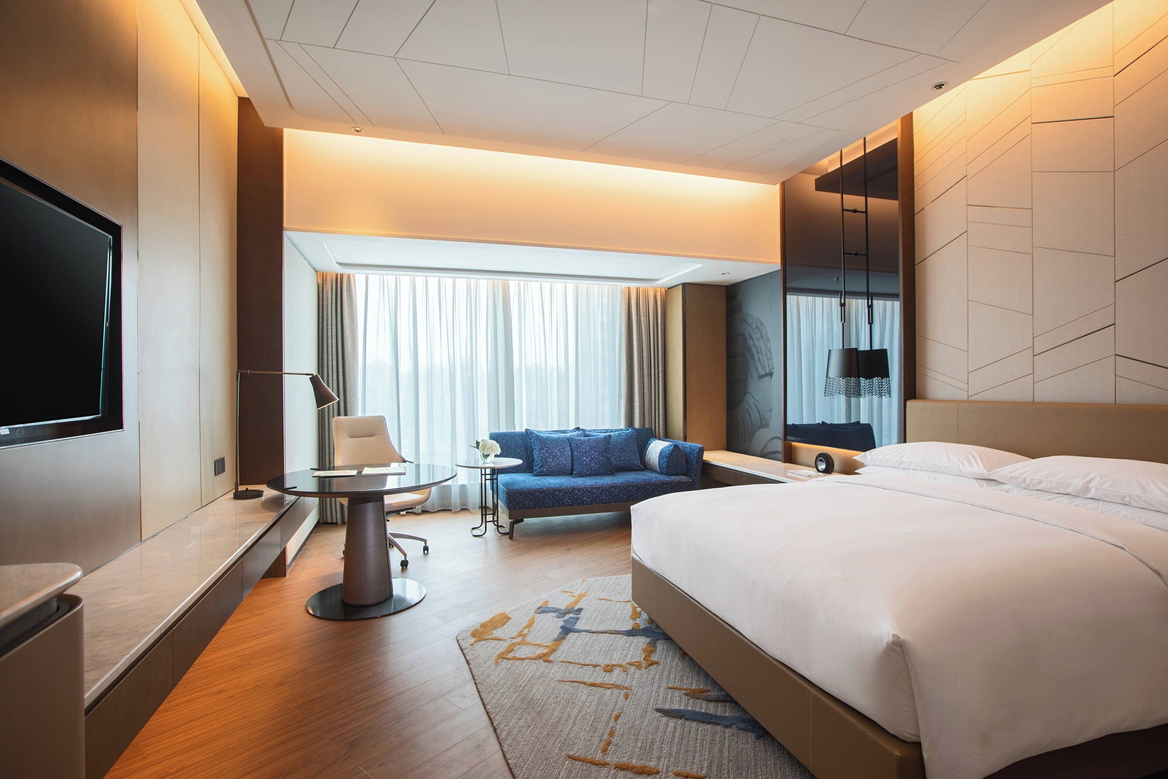 A modern hotel room with a large bed, a sofa, a small table, and a TV.