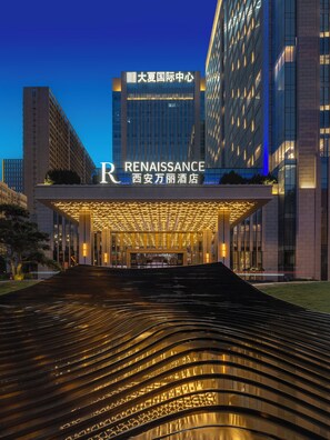 Une entrée d'hôtel moderne, avec une enseigne « Renaissance » bien visible, une façade bien éclairée et un élément décoratif aquatique réfléchissant au premier plan.