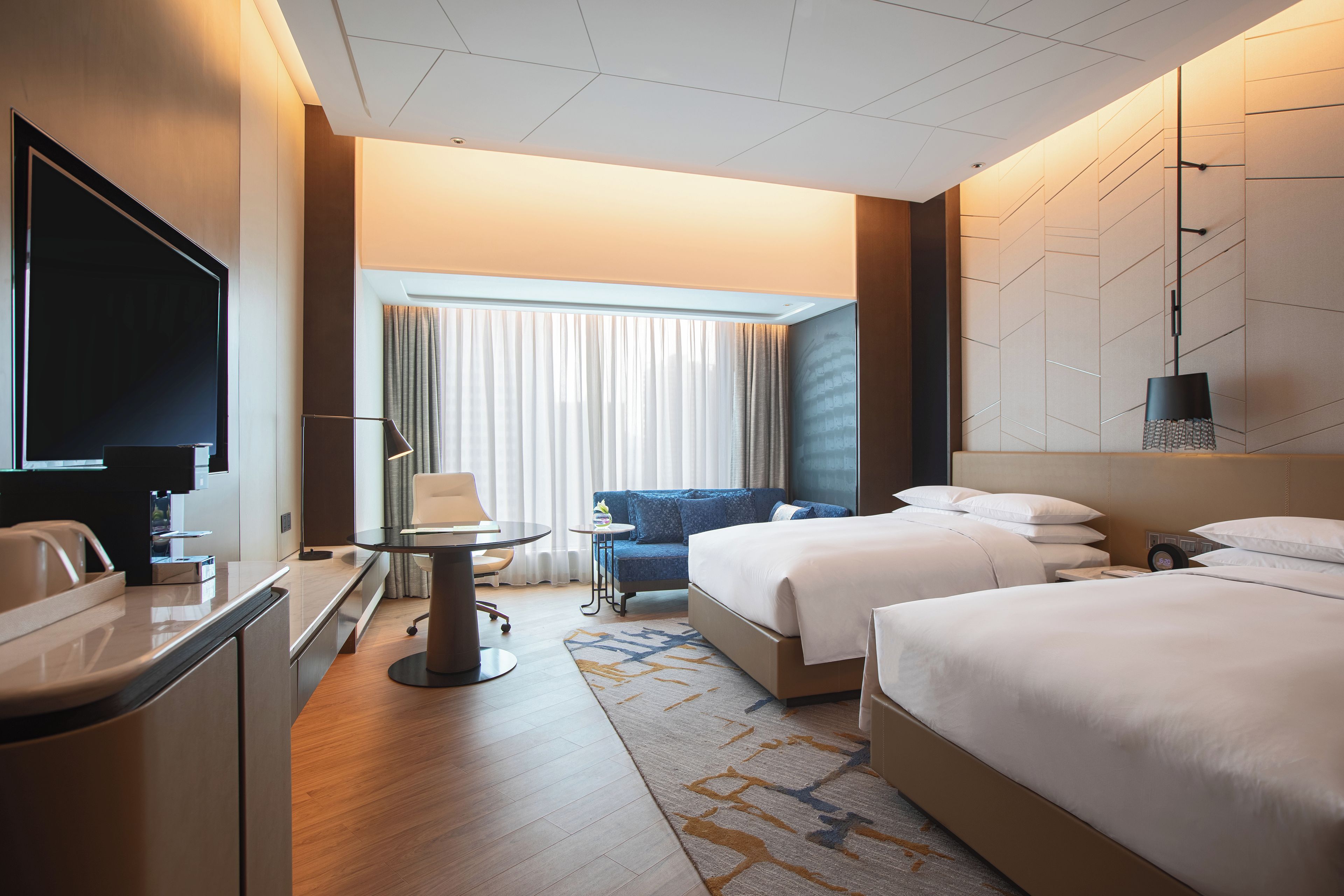 Ein Hotelzimmer mit Schreibtisch, zwei Betten, Fernseher und Blick ins Freie.