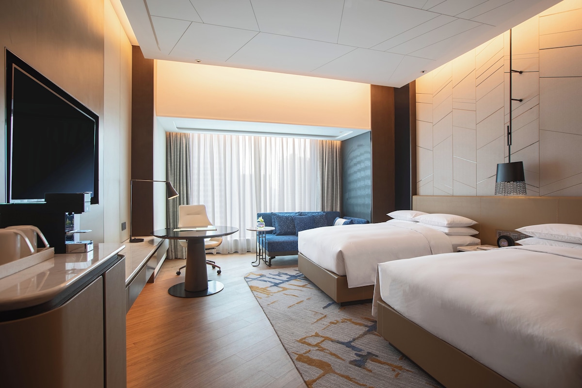Una habitación de hotel con escritorio, dos camas, televisión y vistas al exterior.
