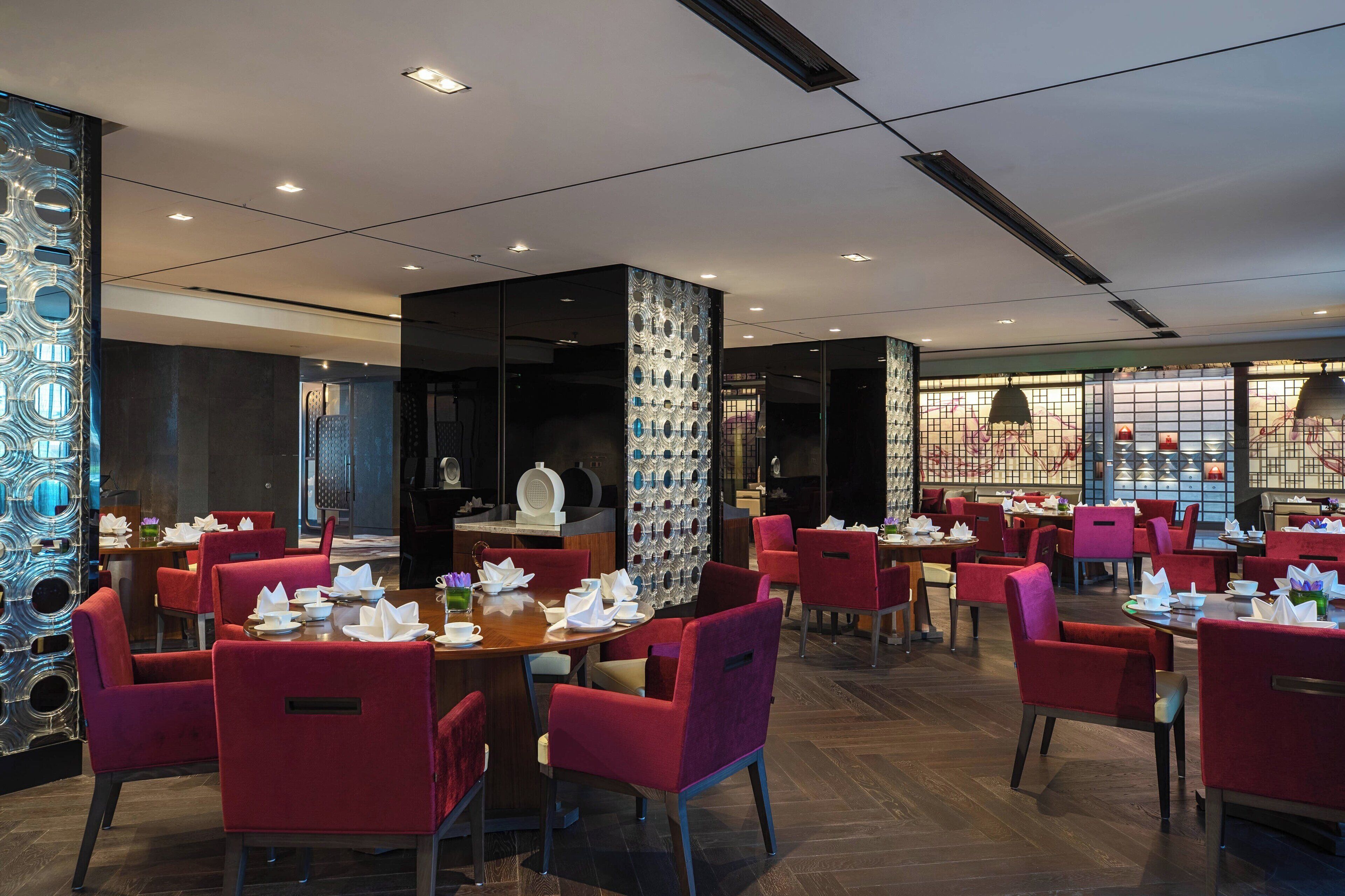 A restaurant with red chairs and tables, a decorative wall, and a modern ceiling design.