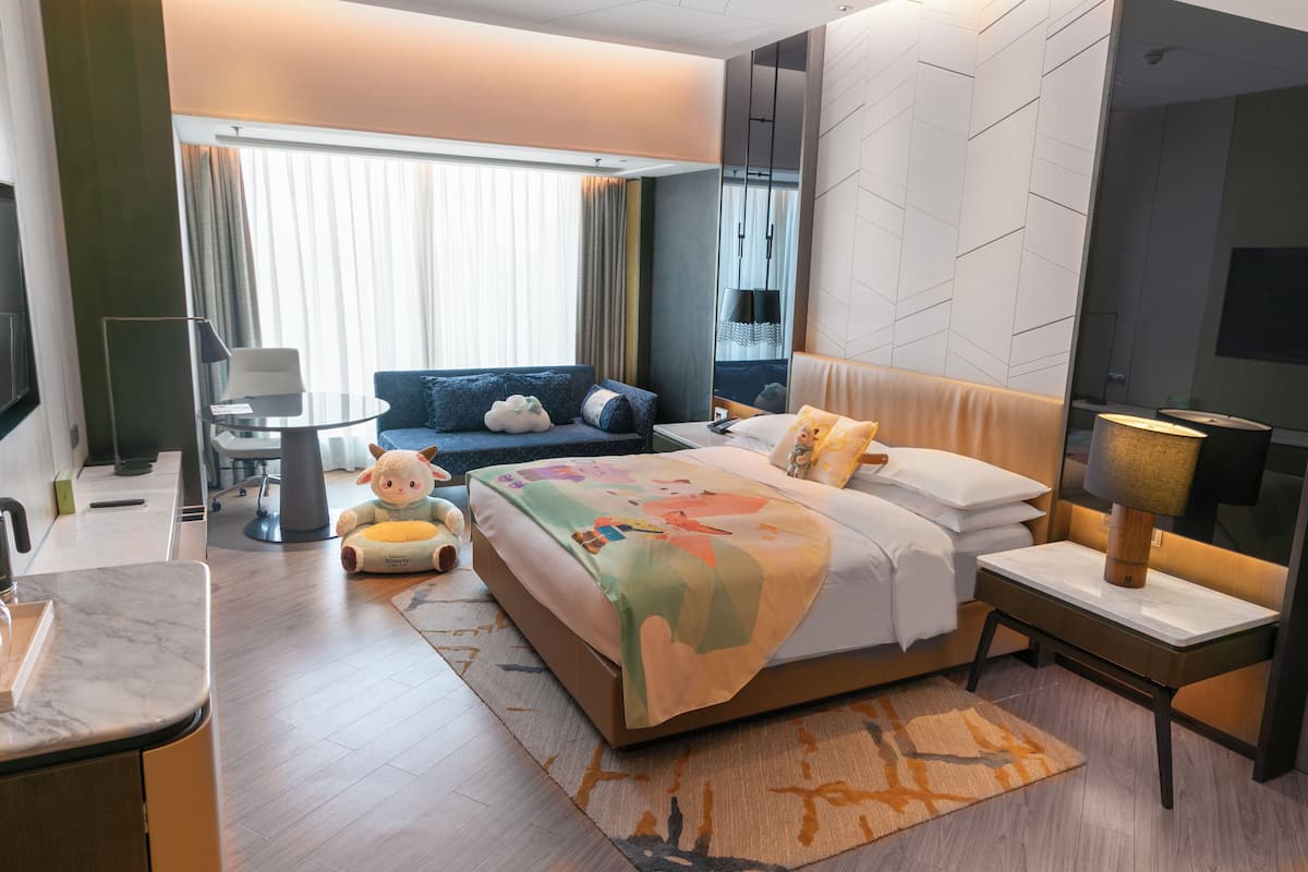A modern hotel room with a large bed, a desk, a sofa, and a small table.
