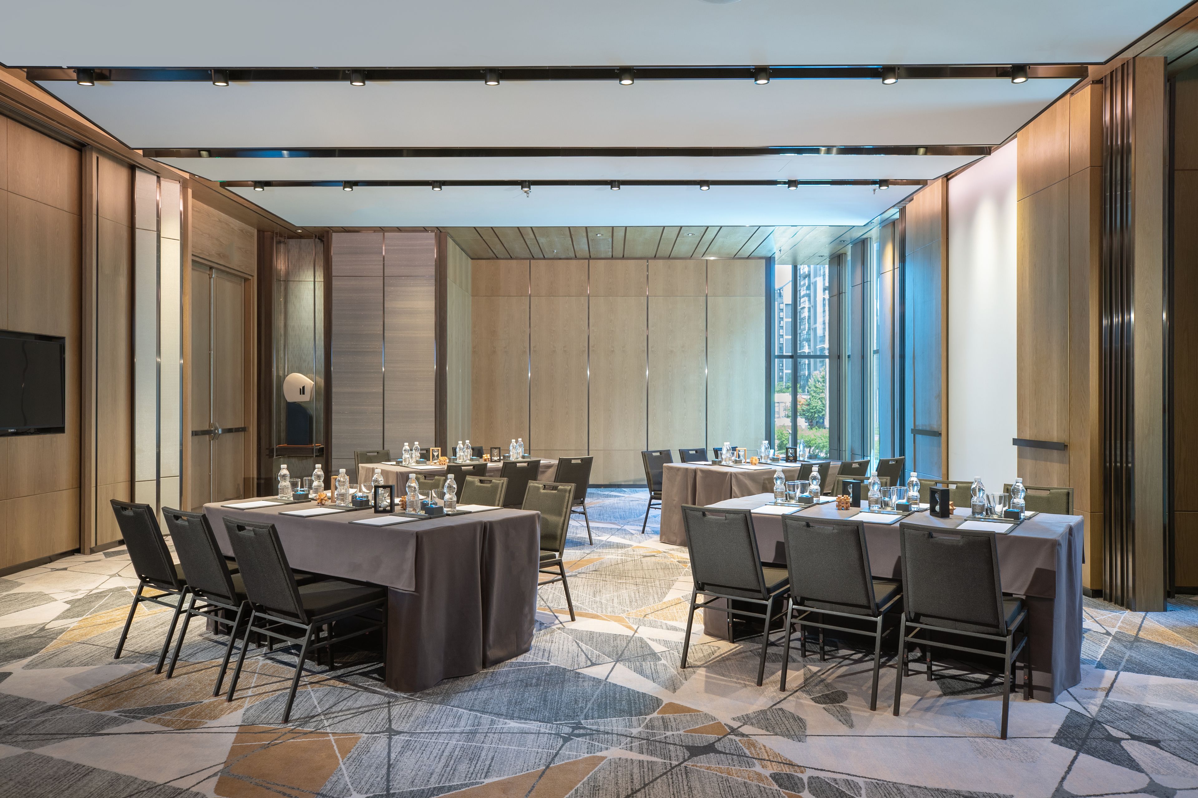 Un salón de conferencias con varias mesas y sillas, ventanas amplias y un diseño moderno.