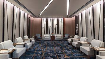 A conference room with a patterned carpet, white chairs, and a central table with a vase of flowers.