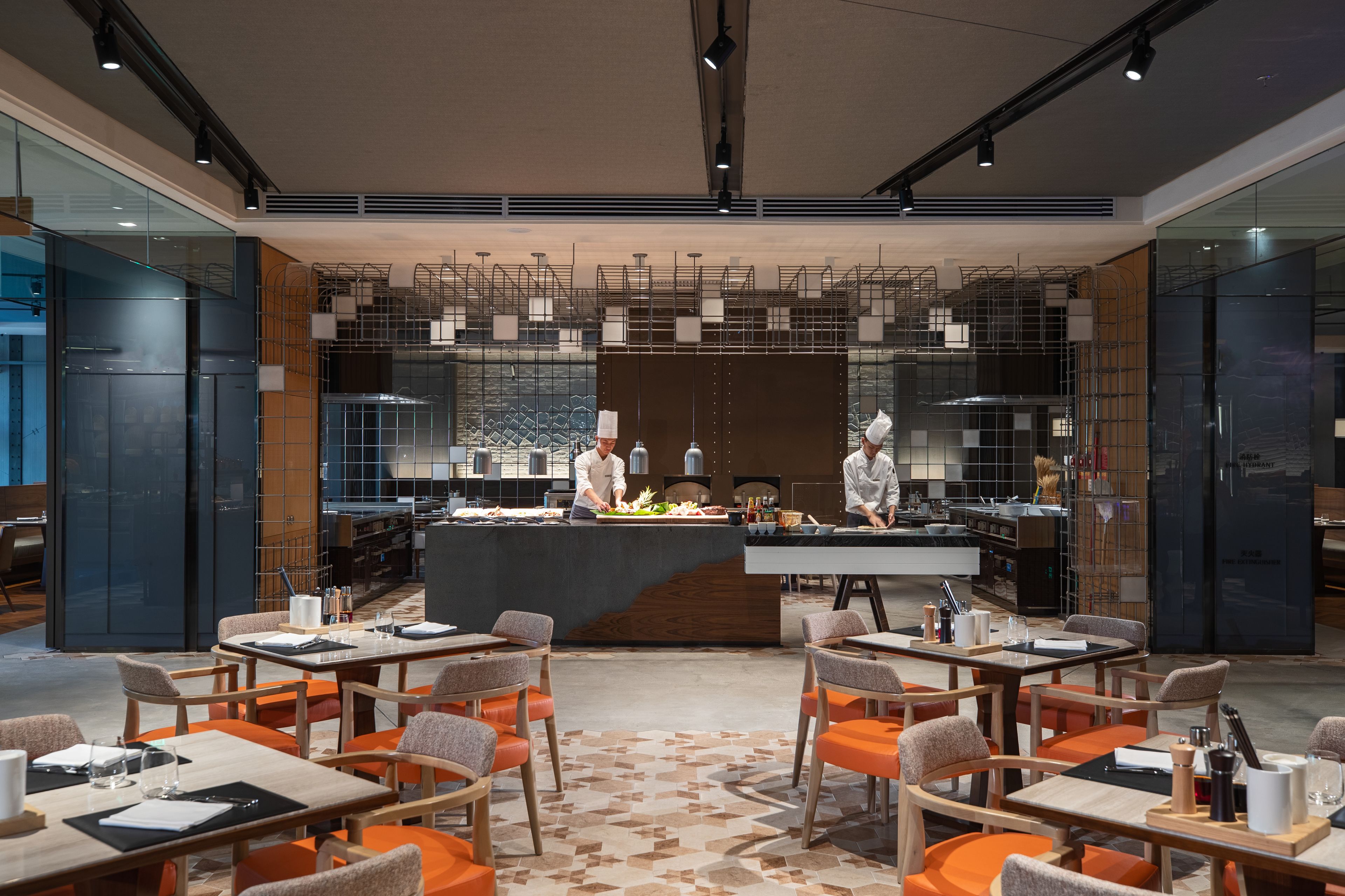 Un restaurante moderno con una barra central, varias mesas de comedor con sillas anaranjadas y un suelo con diseño.