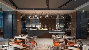 Een modern restaurant met een bar in het midden, meerdere eettafels met oranje stoelen en een vloer met patroon.