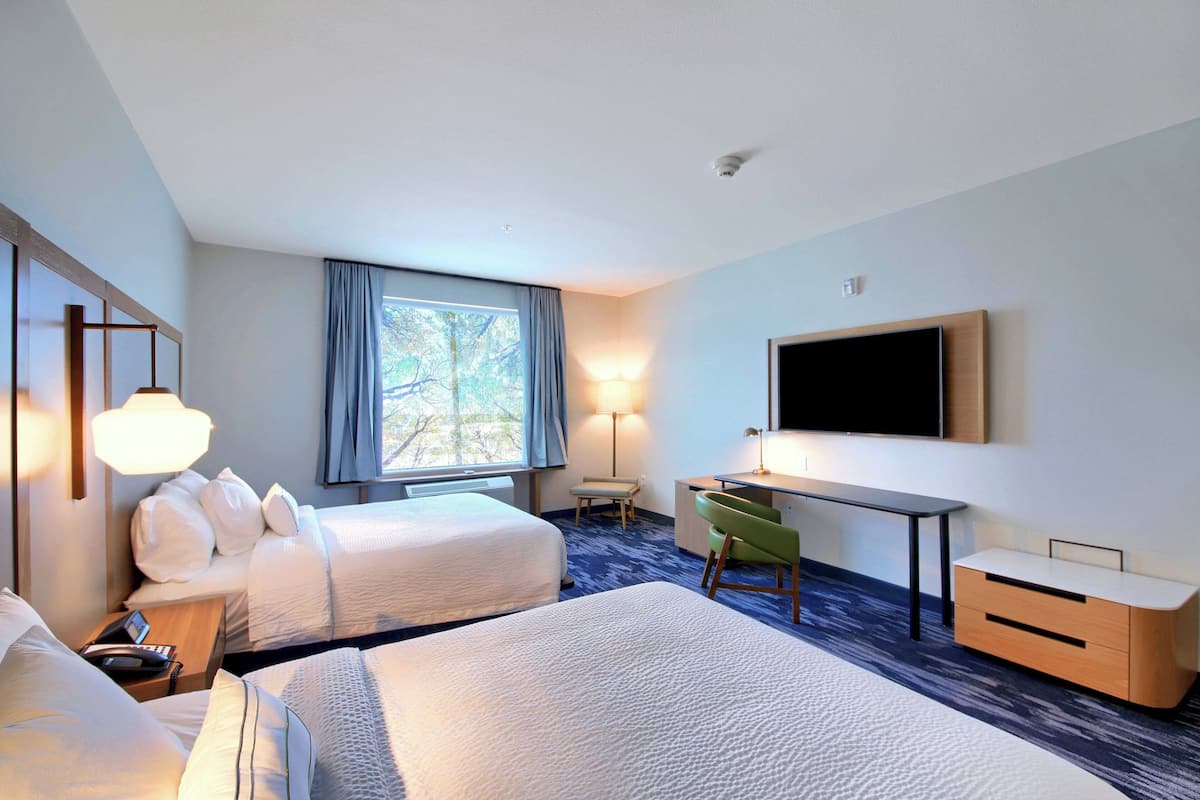 A hotel room with two beds, a desk, a chair, a flat-screen TV, and a window with curtains.