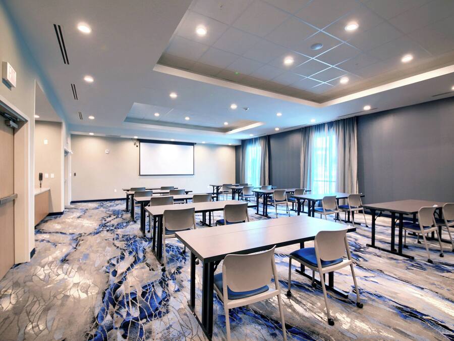 A conference room with tables and chairs, a projector screen, and a carpeted floor.