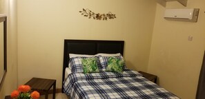 Quarto com cama, mesa de cabeceira, ar-condicionado fixado na parede e um objeto decorativo na parede.
