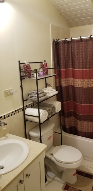 Casa de banho com sanita, lavatório e prateleira com toalhas e artigos de higiene pessoal.