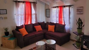 A living room with a sectional sofa, two side tables, a ceiling fan, and a potted plant.