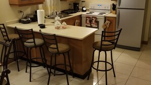 A kitchen with a central island, four bar stools, a refrigerator, a stove, and wooden cabinets.