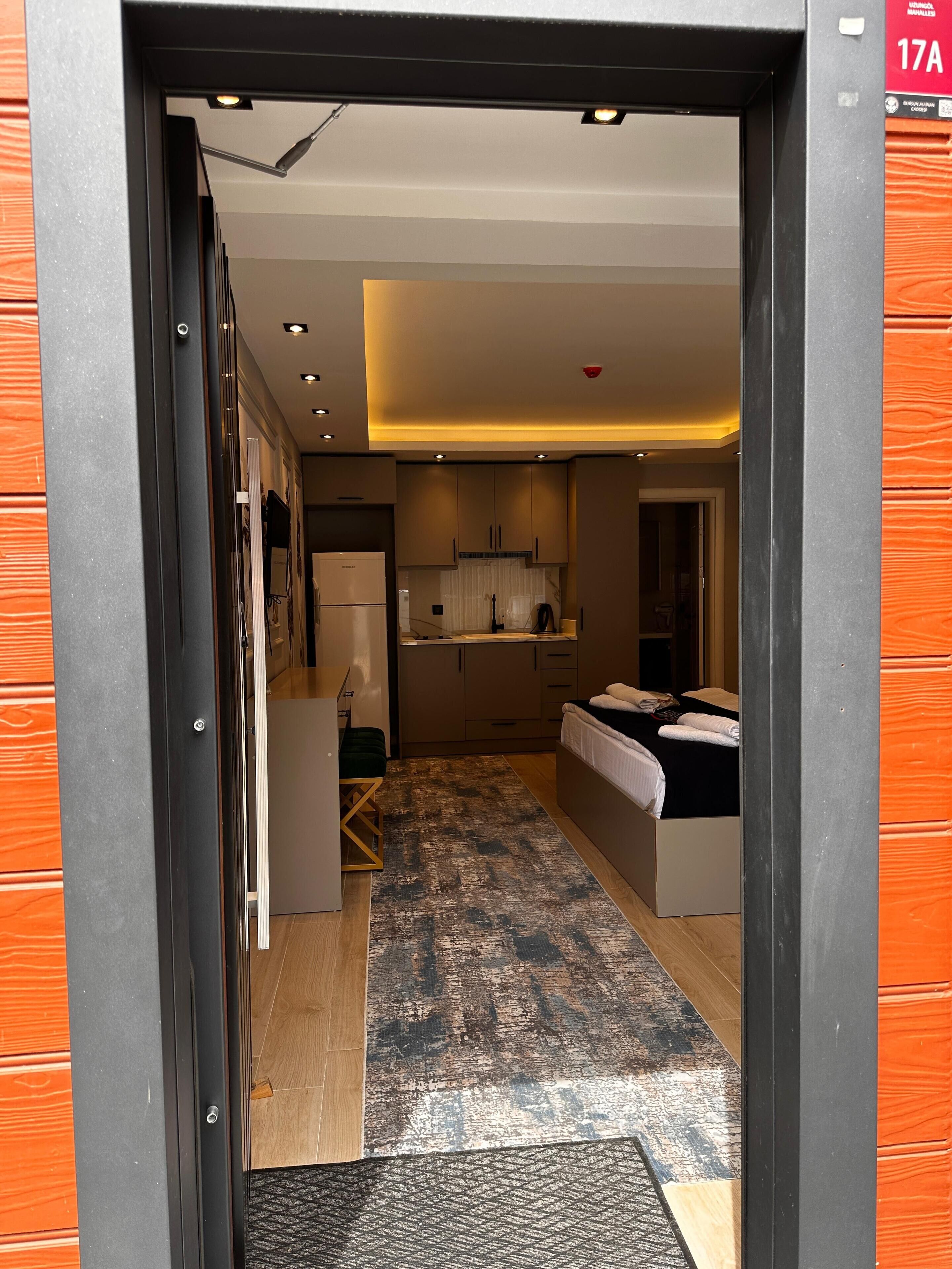 A modern hotel room with a bed, a desk, and a kitchenette.