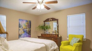 A bedroom with a bed, a bright yellow armchair, a dresser, a ceiling fan, and a painting on the wall. - Lyndale House: Full house with 3 br (Corning)