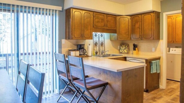 A kitchen with wooden cabinets, a central island with bar stools, a sink, and a dishwasher. - Lyndale House: Full house with 3 br (Corning)