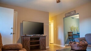 A living room with a TV on a wooden stand, a sofa, a coffee table, and a 'WELCOME' sign in the background. - Lyndale House: Full house with 3 br (Corning)