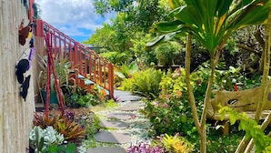 Un camí de jardí amb pedres disposades, envoltat de plantes variades i un pont vermell.