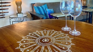 Una taula de fusta amb una petita tela decorativa, dues copes de vi, un sofà amb coixins blaus i un quadre abstracte i colorit a la part superior.