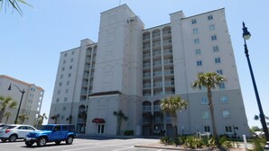 A multi-story hotel with a central tower, balconies, and a parking lot with cars.
