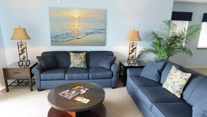 A living room with a sofa set, a coffee table, and two side tables with lamps. There is a painting on the wall and a potted plant.