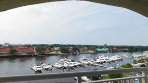 A marina with multiple boats docked, a water tower in the background, and a bridge overhead.