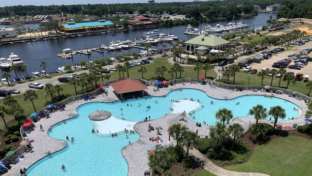 A large outdoor swimming pool with multiple lanes, surrounded by palm trees and a marina with boats.