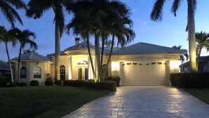 Una propiedad residencial bien iluminada, con entrada pavimentada, palmeras y garaje.