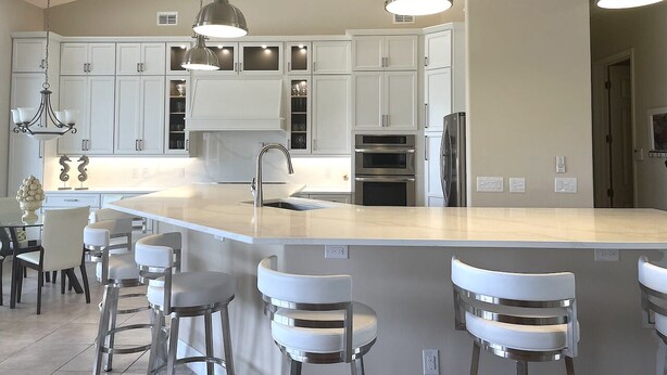 Una cocina moderna con armarios blancos, una isla grande con taburetes de bar, electrodom ésticos de acero inoxidable e iluminación colgante.