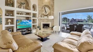 Una sala de estar con televisor, sofás, chimenea y vista a un paisaje tropical.