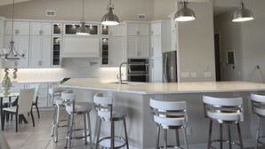 Una cocina moderna con armarios blancos, electrodomésticos de acero inoxidable y una isla central con taburetes de bar.