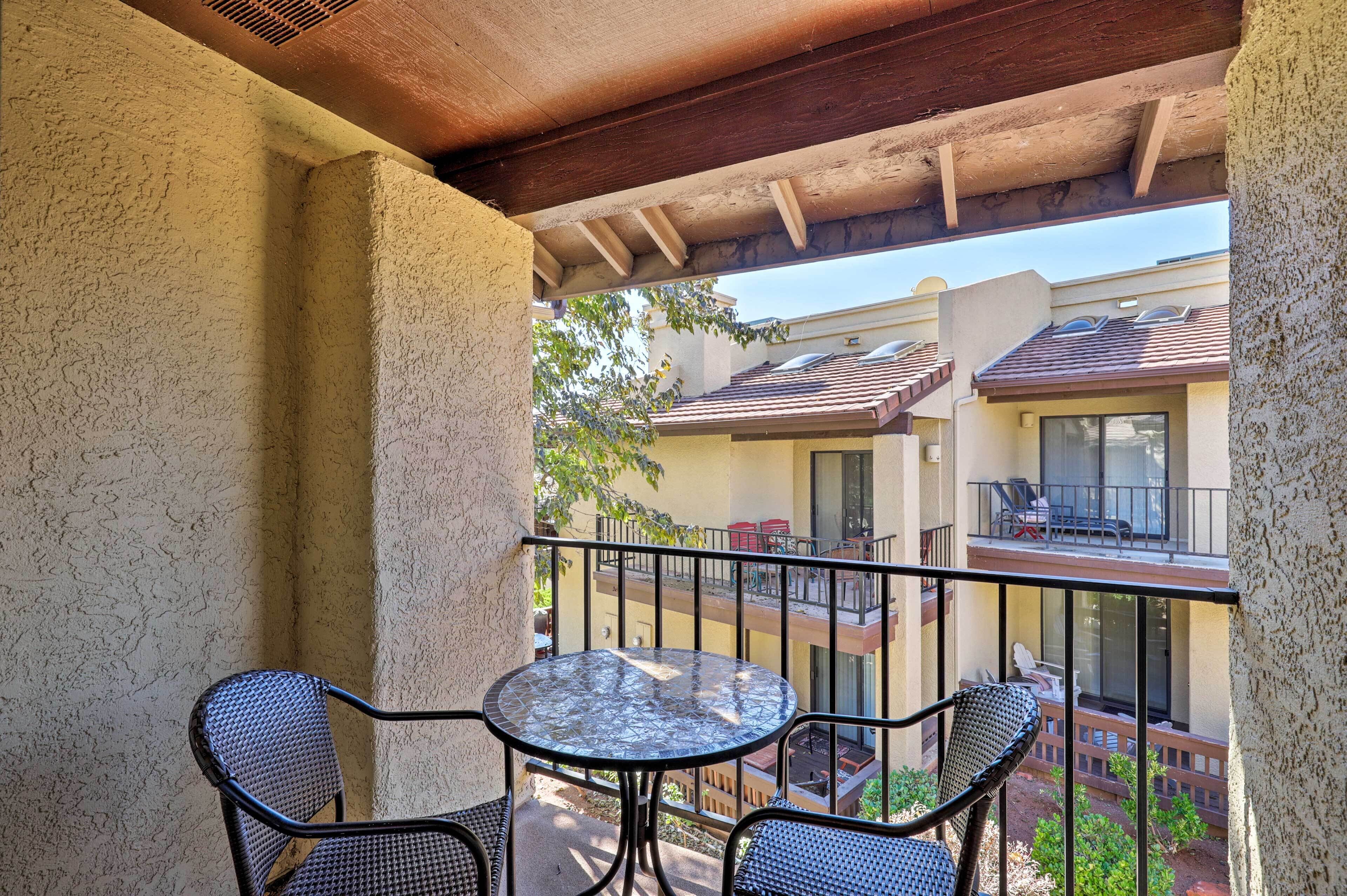 A balcony with a round table and two chairs, overlooking a residential area with multiple buildings.