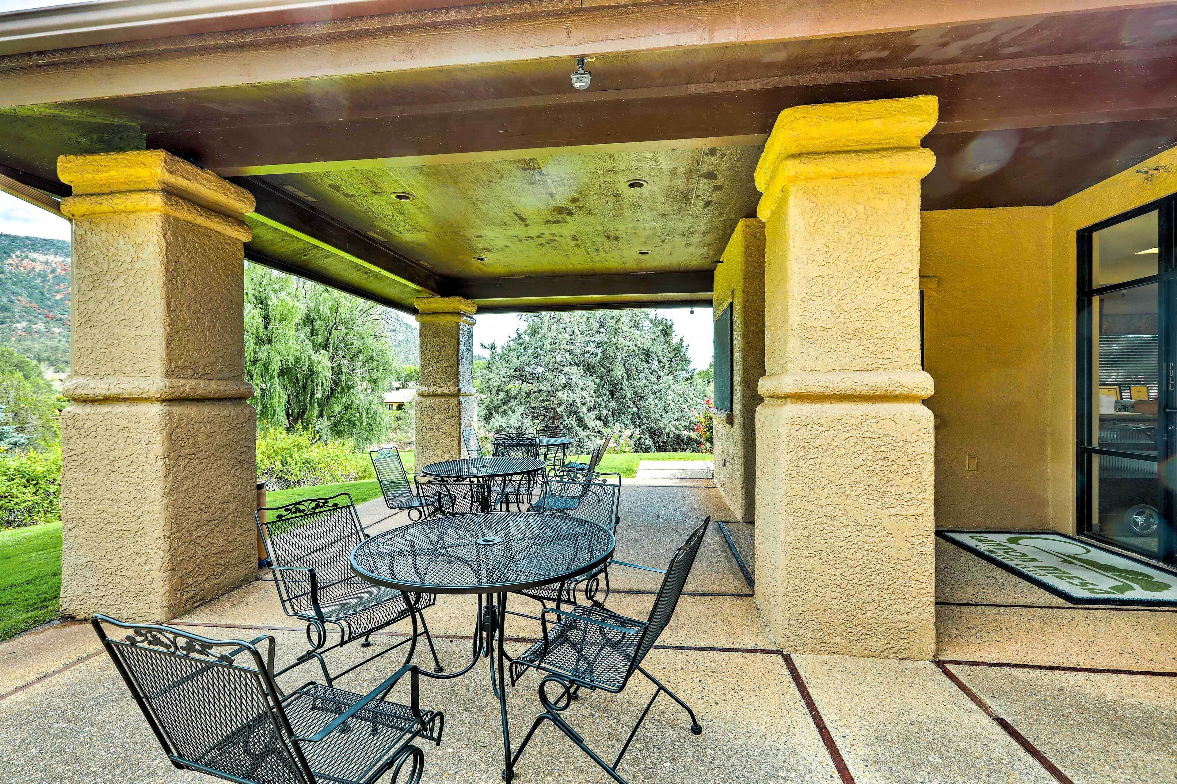 A covered patio area with a round metal table and chairs, surrounded by stone pillars.
