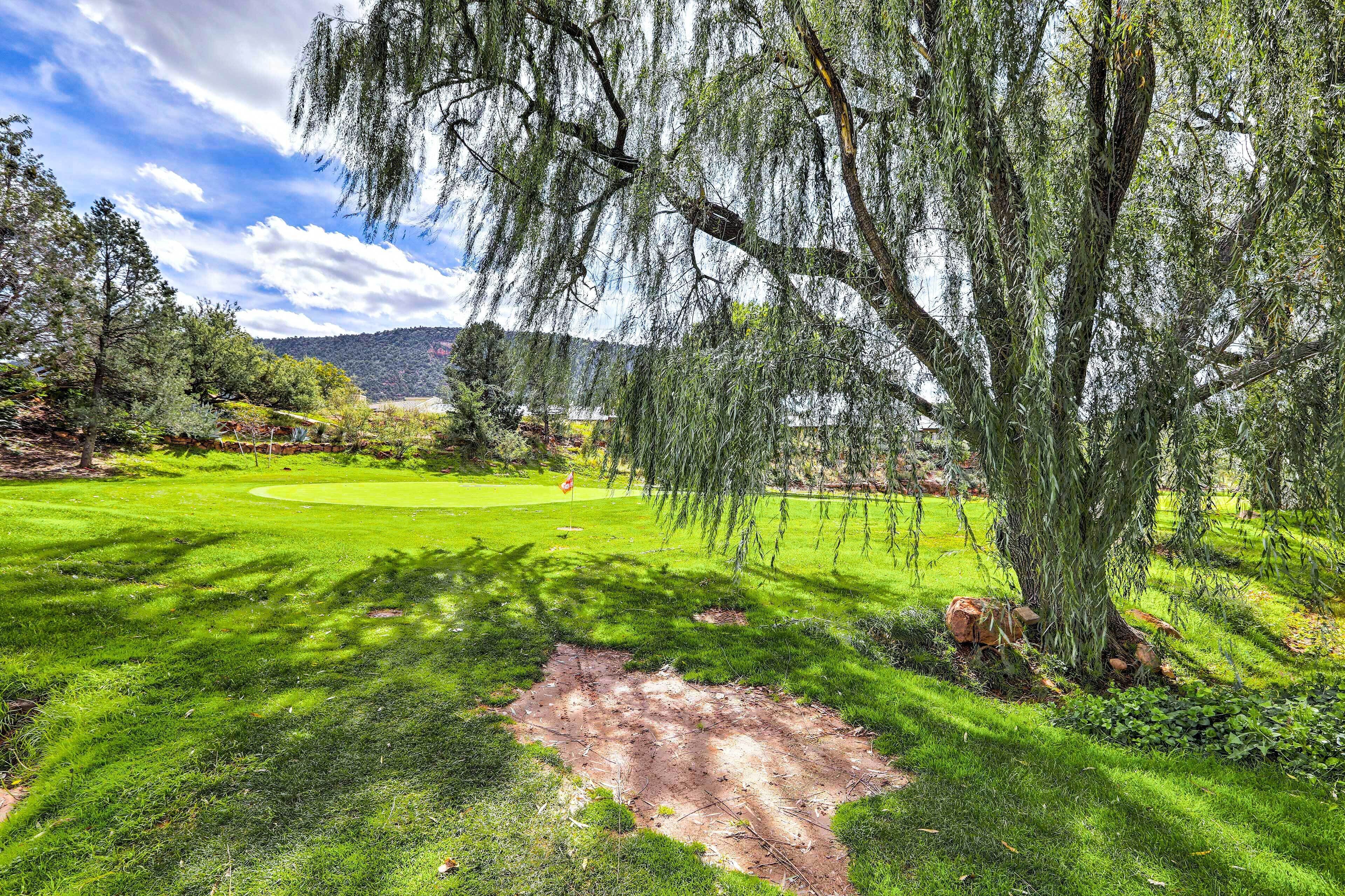 Ein Golfplatz mit einem großen Baum im Vordergrund, einem gepflegten Rasen und einem fernen Gebirgszug unter teils bewölktem Himmel.