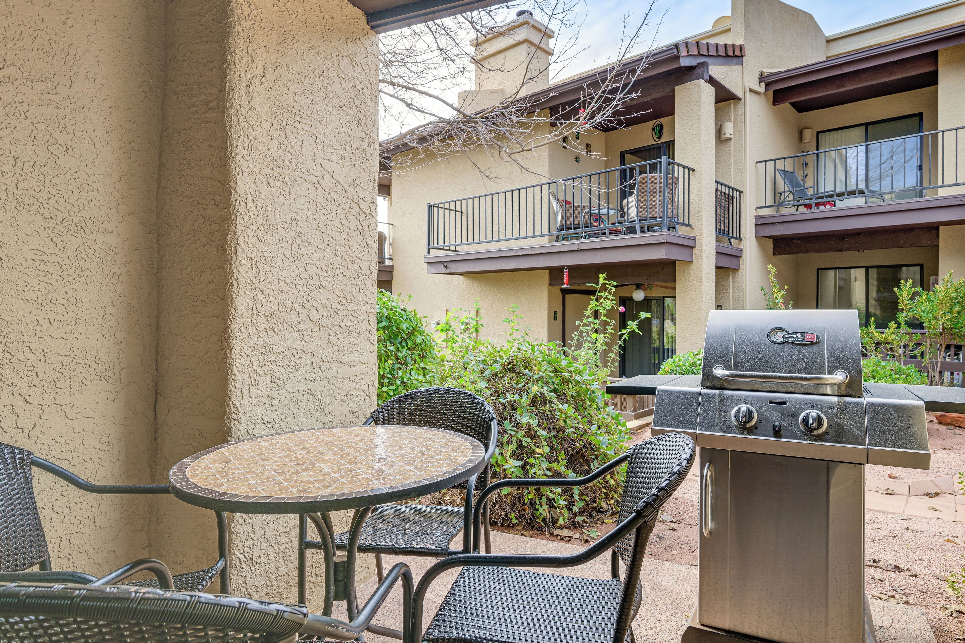 Une terrasse avec une table ronde et des chaises, un barbecue, et un bâtiment avec des balcons en arrière-plan.