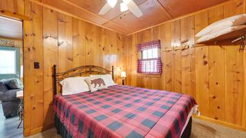 A wooden-paneled bedroom with a bed, a nightstand, a lamp, and a window with plaid curtains.