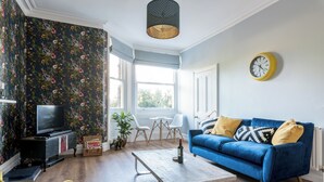 Ein Wohnzimmer mit einem blauen Sofa, einem Holztisch, einem Fernseher und floralem Wandpapier.