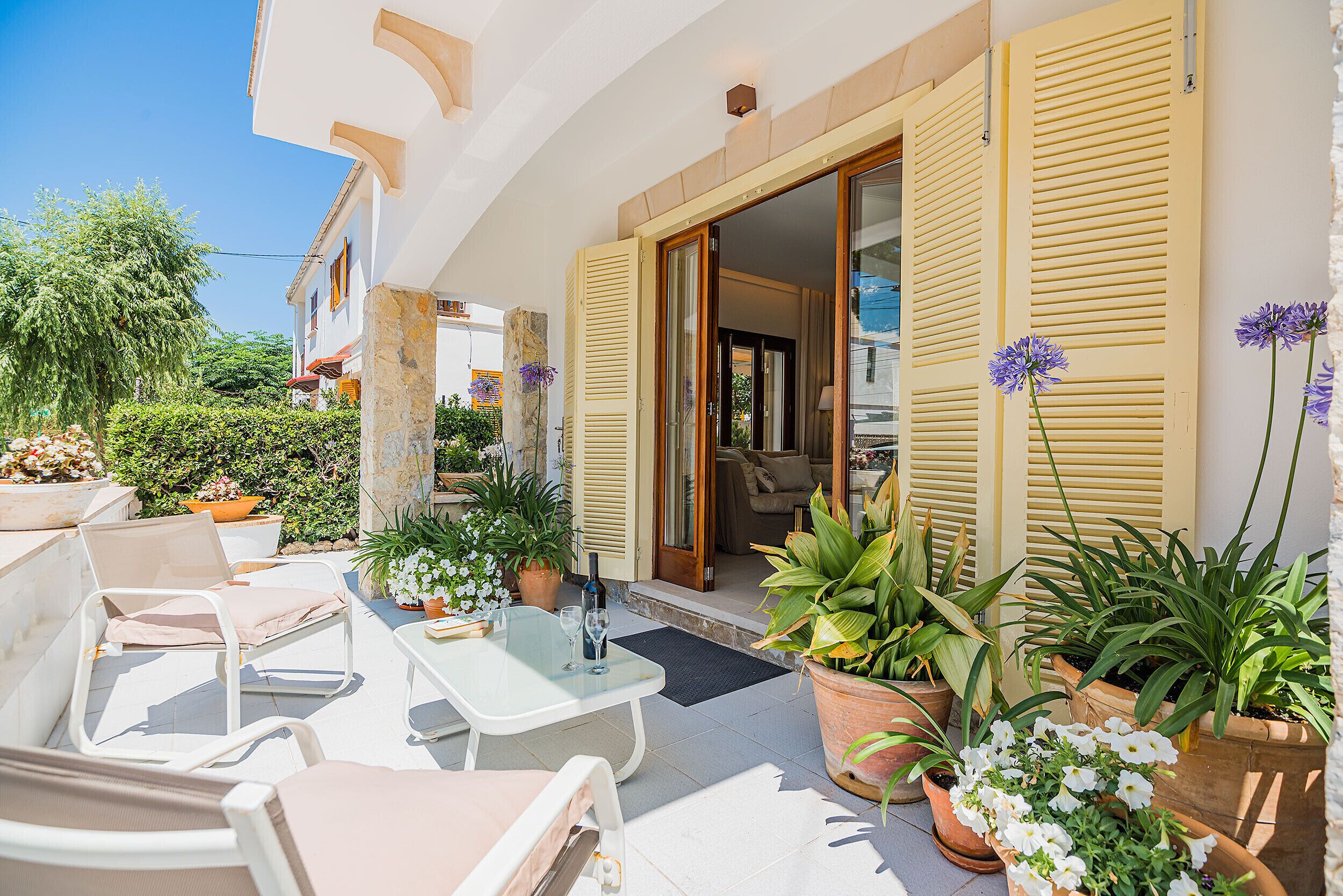 Une terrasse extérieure avec des meubles blancs, des plantes en pot et une porte donnant sur un espace intérieur.