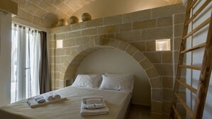 Ein Schlafzimmer mit Steingewölbe über dem Bett, einer Holzleiter und einem Fenster mit Vorhängen.