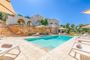 A pool area with stone walls, lounge chairs, and umbrellas.