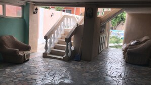 A covered outdoor area with a stone-tiled floor, a white staircase with balustrades, and two wicker chairs. - Villa Keshle Baku (Baku)