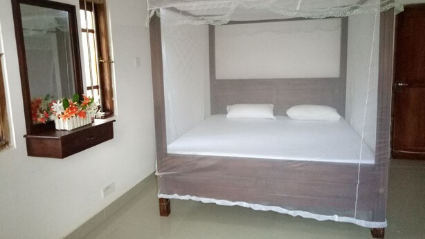 A bedroom with a four-poster bed, a bedside table with a mirror, and a window with a view. - Villa Hilltop (Hikkaduwa)