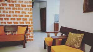 A living room with a brick-patterned wall, a wooden sofa with orange cushions, a wooden table, and a patterned cushion. - Villa Hilltop (Hikkaduwa)