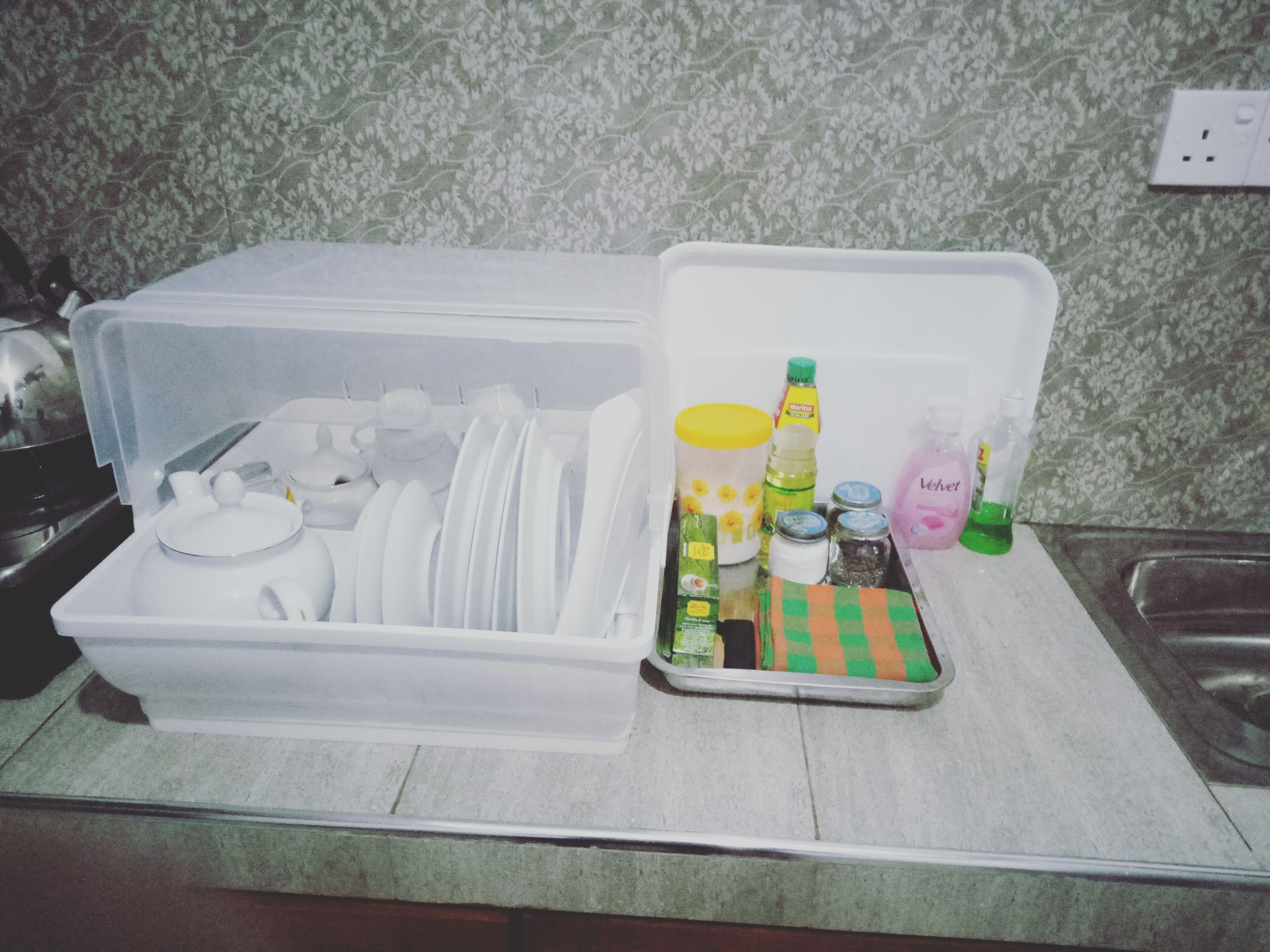 Una cocina con un recipiente de almacenamiento que contiene vajilla y una bandeja con condimentos y productos de limpieza.