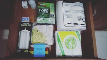 Un cajón con varios objetos, incluyendo una vela, un paquete de papel higiénico, una caja de pañuelos y un paquete de toallitas.