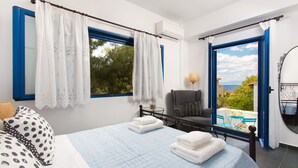 A bedroom with a bed, a chair, a table, and a view of the outdoors. - Seaside Luxury Villa with Terrace in Aegina Island | Aneli Villa Aegina (Aegina)