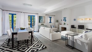 A modern living room with a dining area, white furniture, and a fireplace. - Seaside Luxury Villa with Terrace in Aegina Island | Aneli Villa Aegina (Aegina)