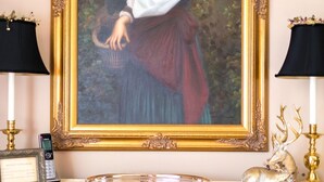 A framed portrait on a wooden table with two lamps, a decorative plate, and a small animal figurine.